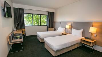 Une chambre d’hôtel avec deux lits, un bureau, une chaise, une télévision et une fenêtre avec des rideaux.