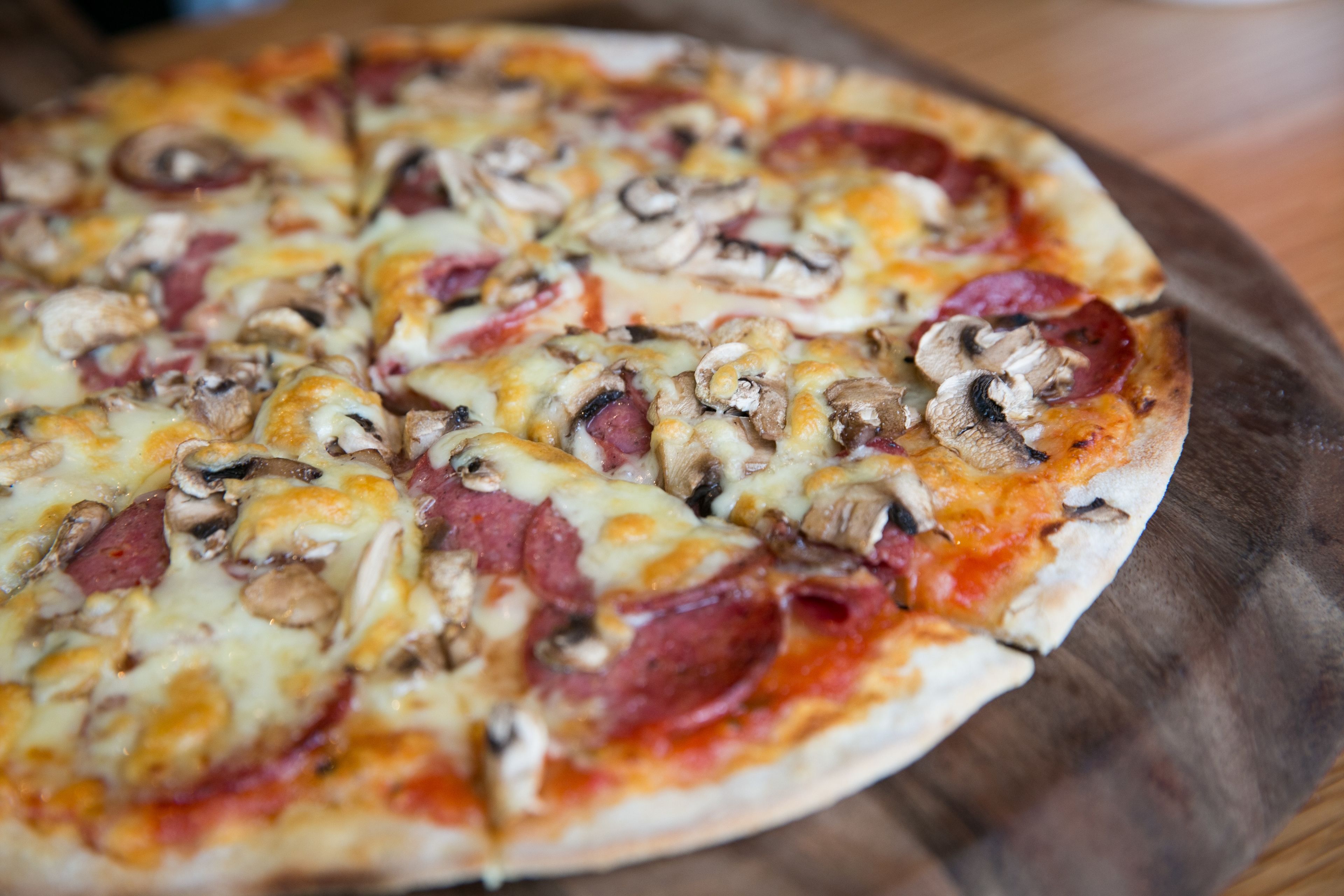 A pizza with pepperoni and mushrooms on a wooden board.