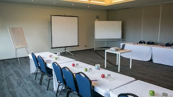 Una sala de conferencias con una mesa larga, sillas, una pantalla de proyector y una pizarra.