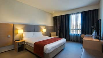 A hotel room with a large bed, two bedside lamps, a desk with a chair, and a TV.