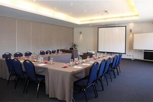 Una sala de conferencias con una larga mesa, sillas, una pantalla de proyector y un atril.
