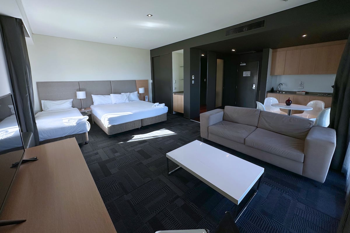 Ein Hotelzimmer mit zwei Betten, einem Schlafsofa, einem Couchtisch und einer Küchenzeile.