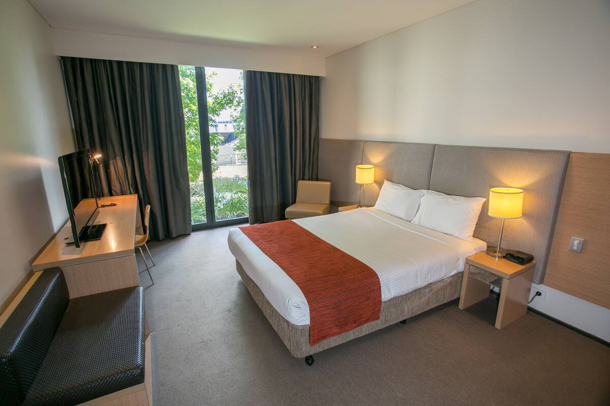 Ein Hotelzimmer mit einem Bett, Nachttischen, einem Schreibtisch, einem Sessel und einem Fernseher.