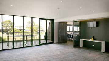 A spacious room with large windows, a white console table, and a flat-screen TV mounted on the wall.