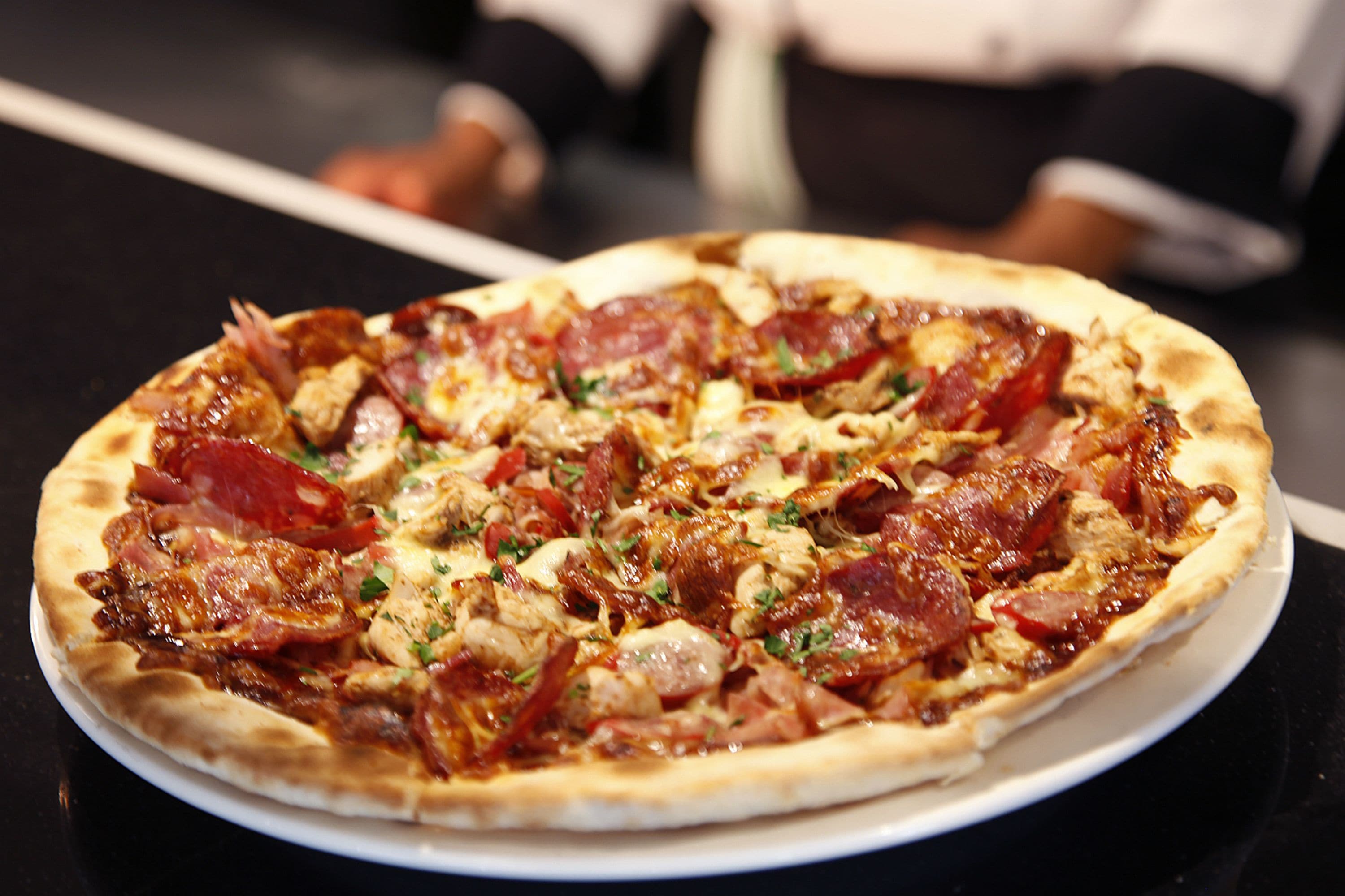 Una pizza con pepperoni y pollo sobre un plato blanco.