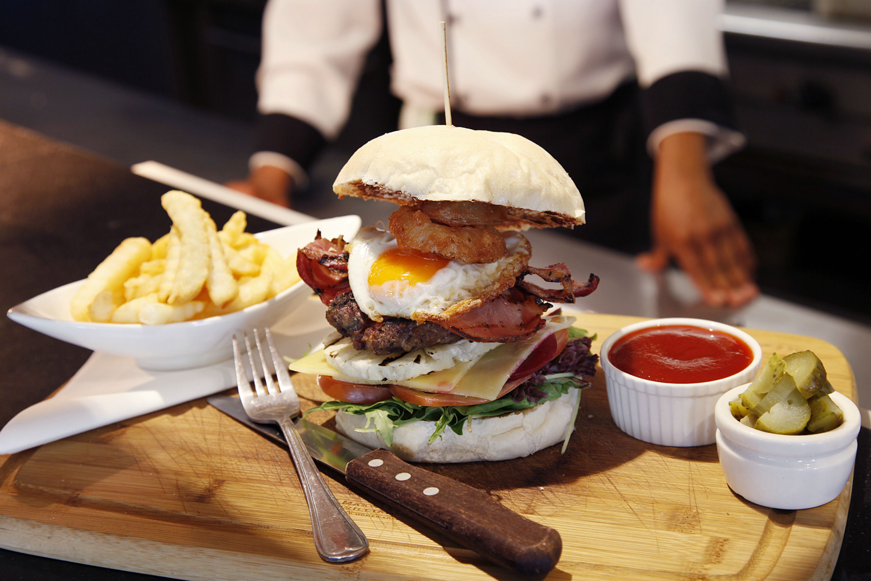 A meal with a burger, fries, and a drink on a wooden board.