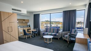 Habitación de hotel moderna con una cama grande, un sofá, una mesa de comedor y una cocina.