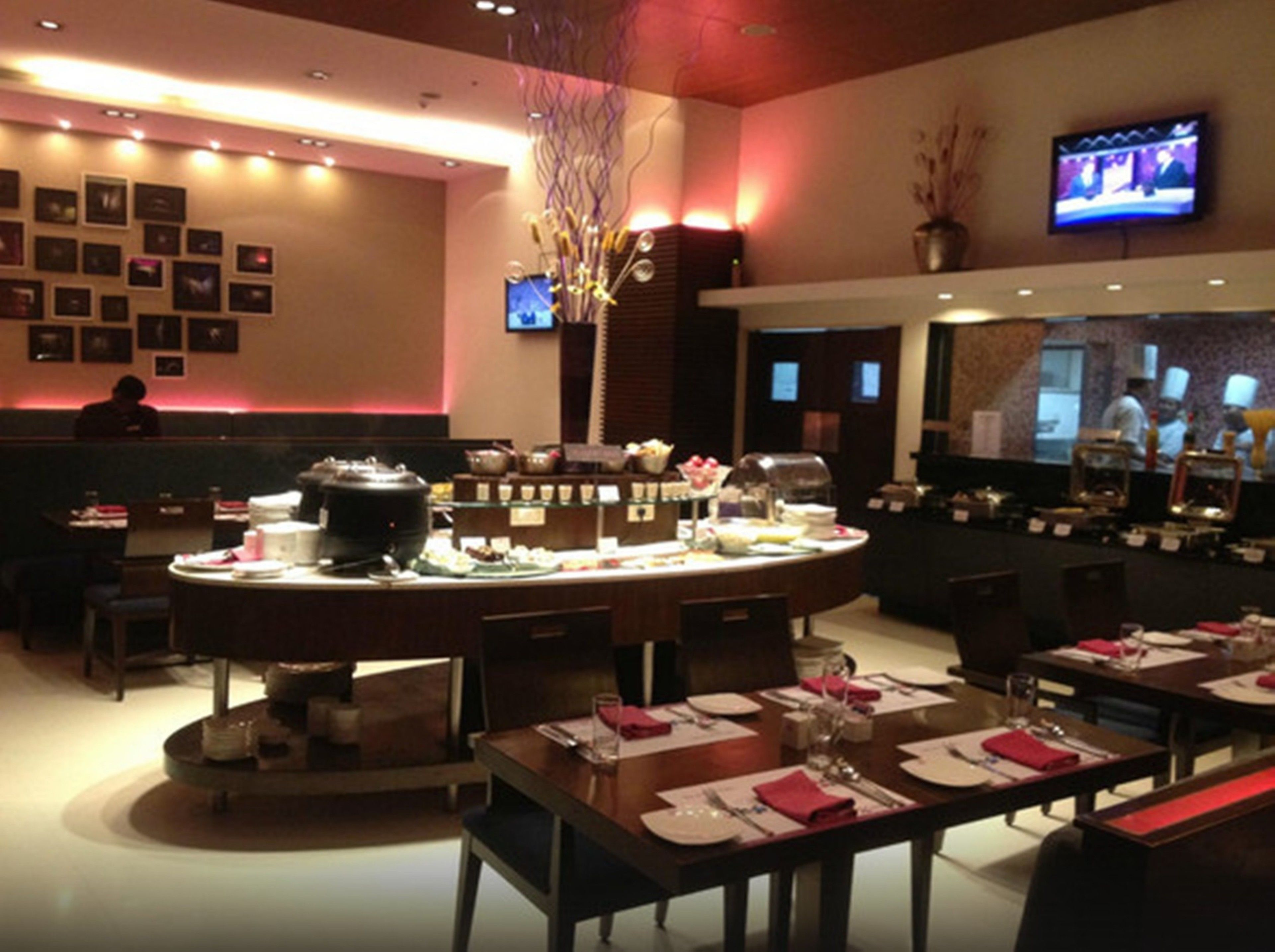 A restaurant with a buffet setup, multiple dining tables, and a television mounted on the wall.