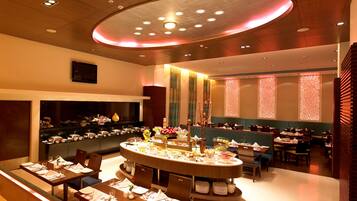 Un comedor moderno con una mesa redonda central, varios arreglos de asientos y elementos decorativos como flores y paneles con diseños.