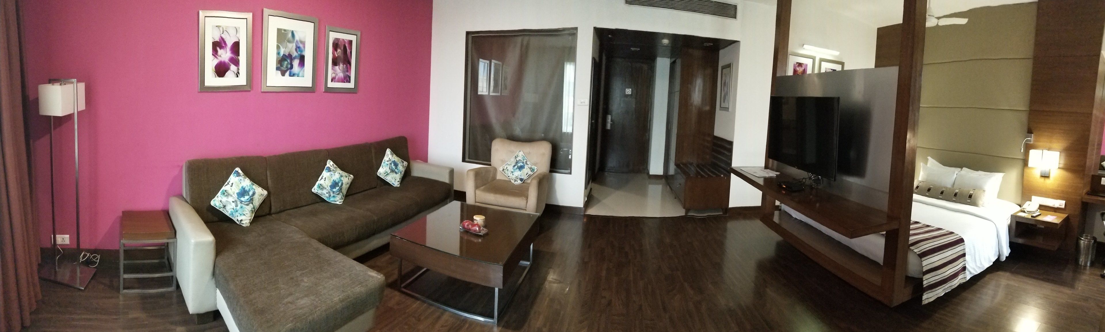 Una sala de estar con un sofá marrón, una mesa de centro de vidrio, un televisor y una cama con una manta a rayas.