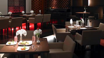 Un restaurante con poca luz y mesas dispuestas para comer, con una decoración moderna que incluye detalles en rojo y paneles decorativos.