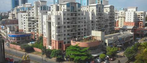 A multi-story residential building with a central courtyard, surrounded by other buildings and a street with vehicles and pedestrians.