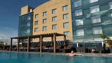 A swimming pool with lounge chairs and a covered seating area, adjacent to a modern building with large windows.