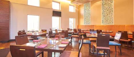 Une salle de conférence dotée de plusieurs tables et chaises, de grandes fenêtres et d’un panneau mural décoratif.