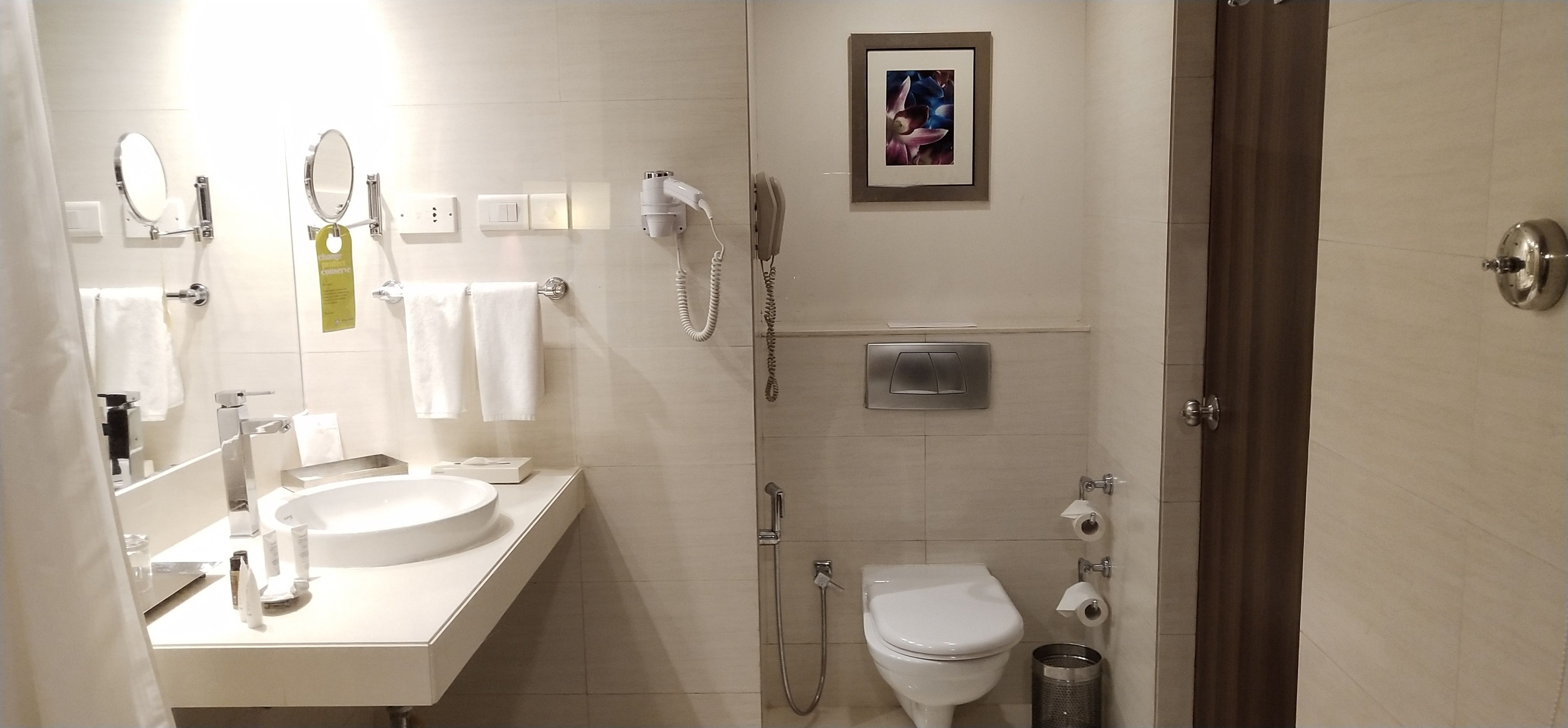 A modern bathroom with a sink, mirrors, a toilet, a shower, and a hairdryer.