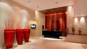 A modern reception area with a black reception desk, red decorative vases, and a television screen on the wall. - Royal Orchid Central Pune (Pune)