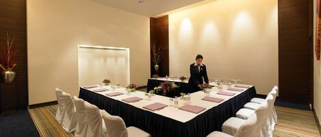 Un salón de conferencias con una larga mesa dispuesta para una reunión, rodeado de sillas.