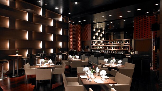 A modern restaurant with a dark interior, wooden panel walls, and a bar area with shelves of bottles. - Royal Orchid Central Pune (Pune)