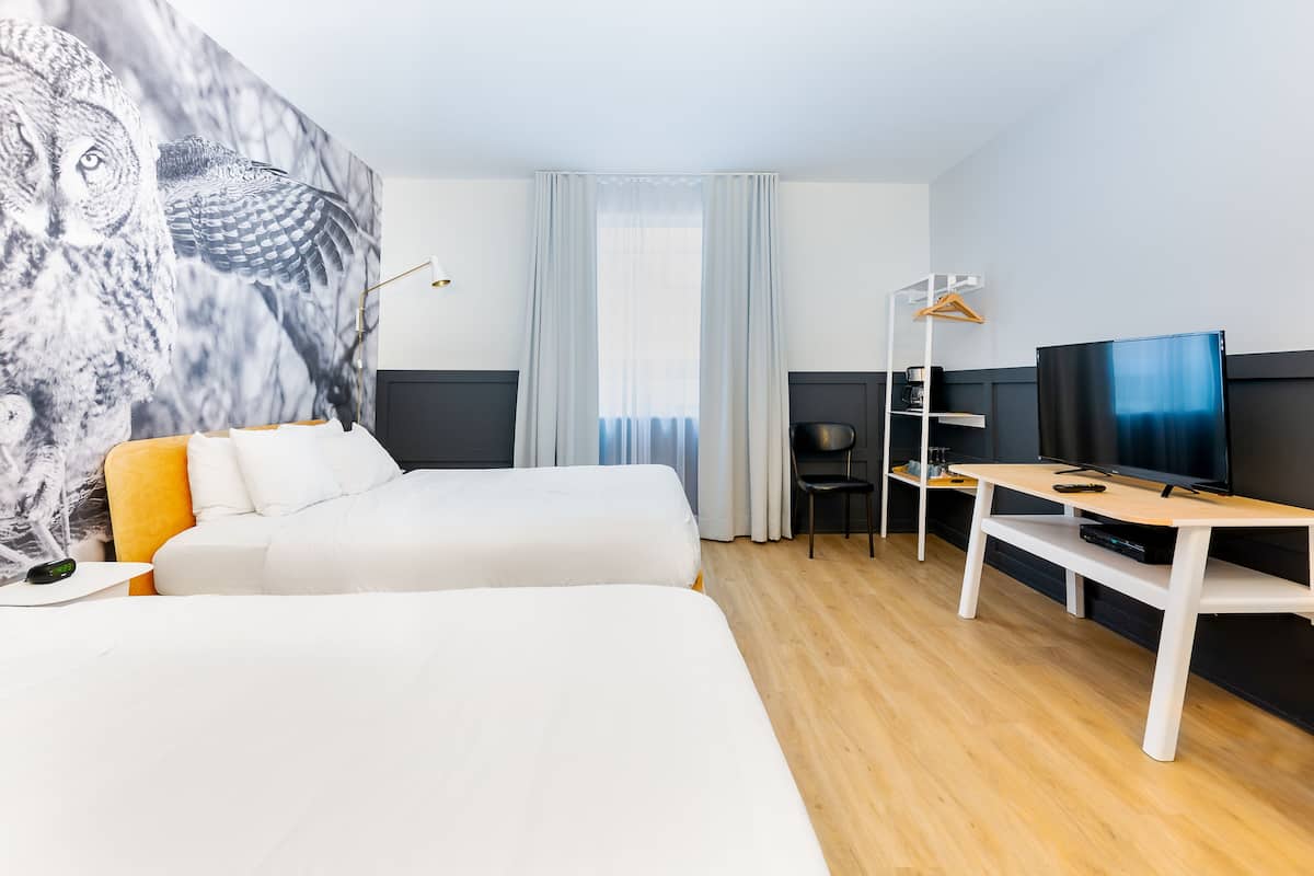 A hotel room with two beds, a desk with a TV, a chair, and a wall-mounted TV.
