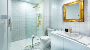 A modern bathroom with a glass-enclosed shower, a white toilet, and a vanity with a gold-framed mirror. - Hôtel du Jardin by Les Lofts Vieux-Quebec (Québec City)