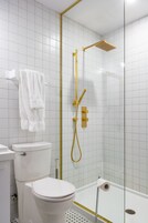 Ein Badezimmer mit Toilette und Waschbecken in Weiß sowie einer Duschkabine mit Goldarmaturen.