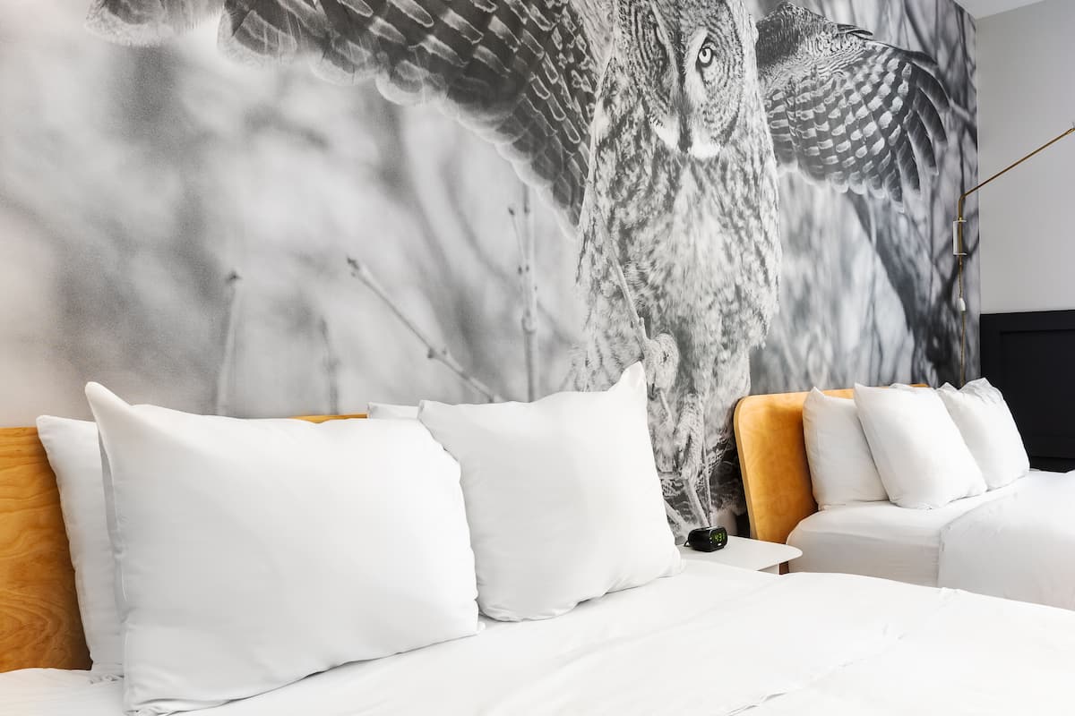 A bedroom with a large wall mural of an owl, white bedding, and a modern headboard.