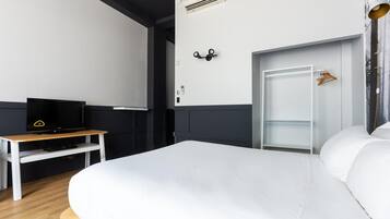 Une chambre d’hôtel moderne avec un grand lit, un téléviseur à écran plat posé sur une table en bois, une armoire et une porte dotée d’un porte-manteau.
