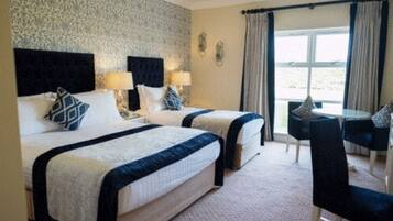 A hotel room with two beds, a dining area with a table and chairs, and a view of the outdoors through large windows.