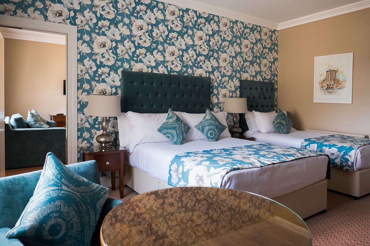 Une chambre d’hôtel avec deux lits, un papier peint à motifs floraux, une table ronde et un canapé.