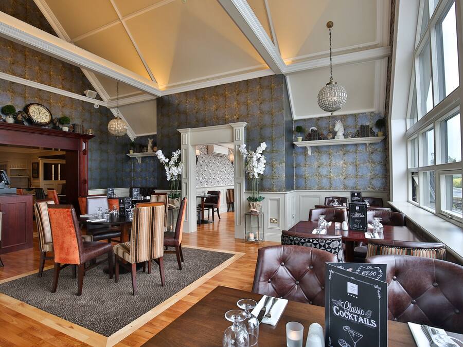 A spacious dining area with high ceilings and large windows, featuring a variety of seating arrangements and a menu board.