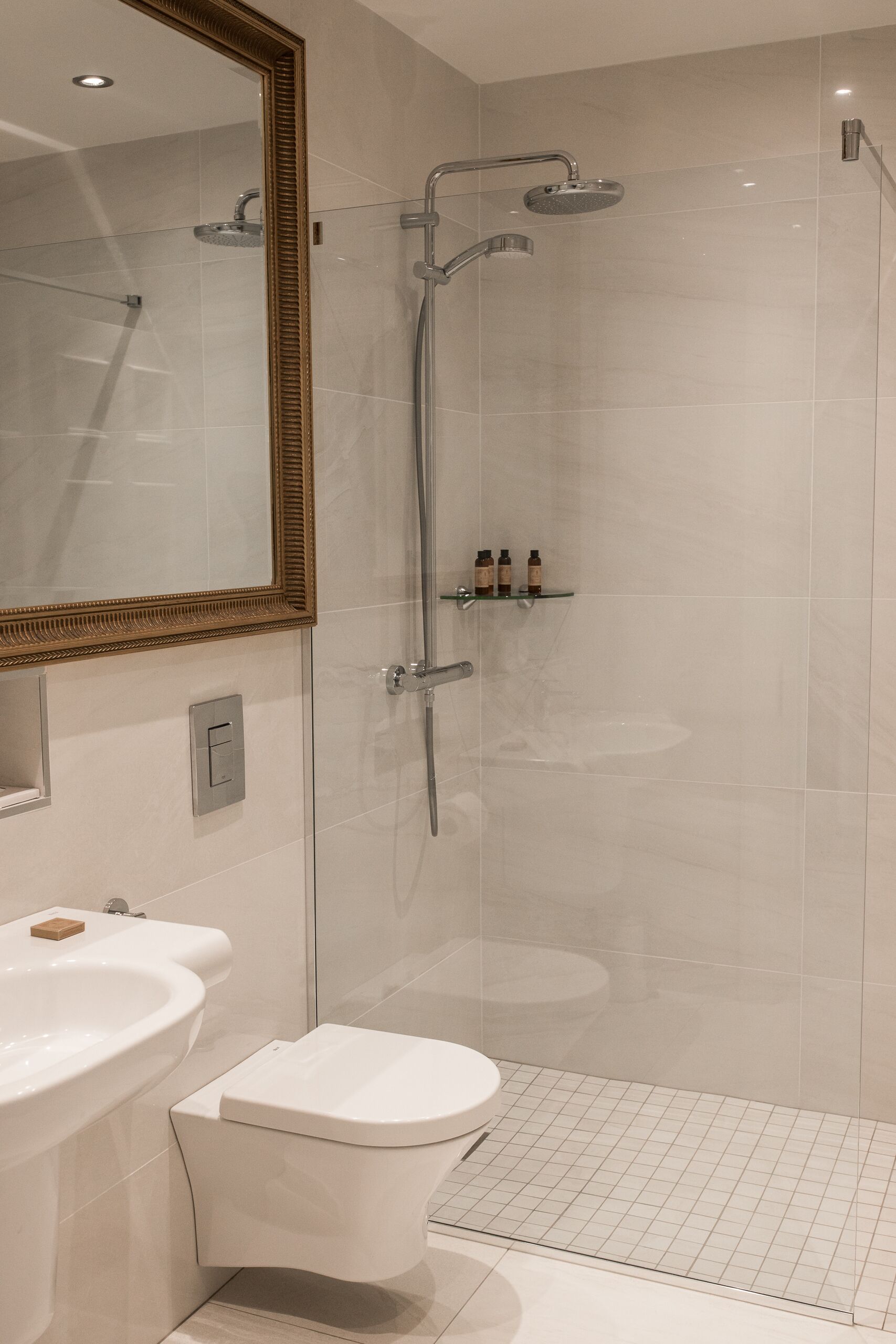 Un baño moderno con ducha envuelta en vidrio, inodoro blanco y lavamanos con jabonera.