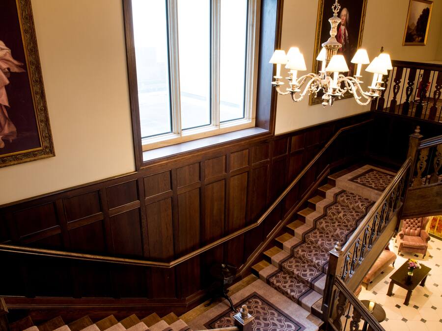 A grand staircase with a patterned carpet, a chandelier, and a framed portrait on the wall.