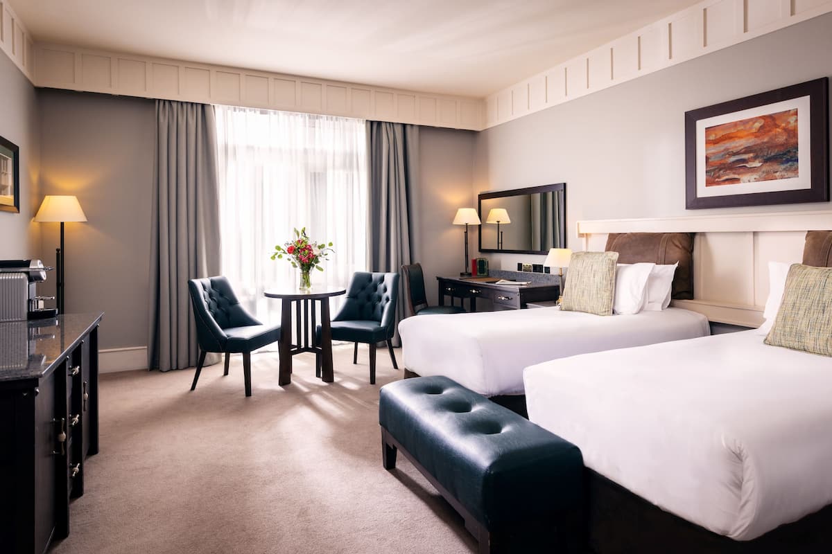 A hotel room with two beds, a desk, a chair, a TV, and a painting on the wall.