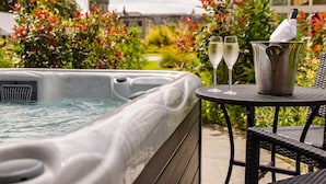 A hot tub with two glasses of champagne on a table, surrounded by lush greenery and a building in the background. - Lough Eske Castle (Donegal)