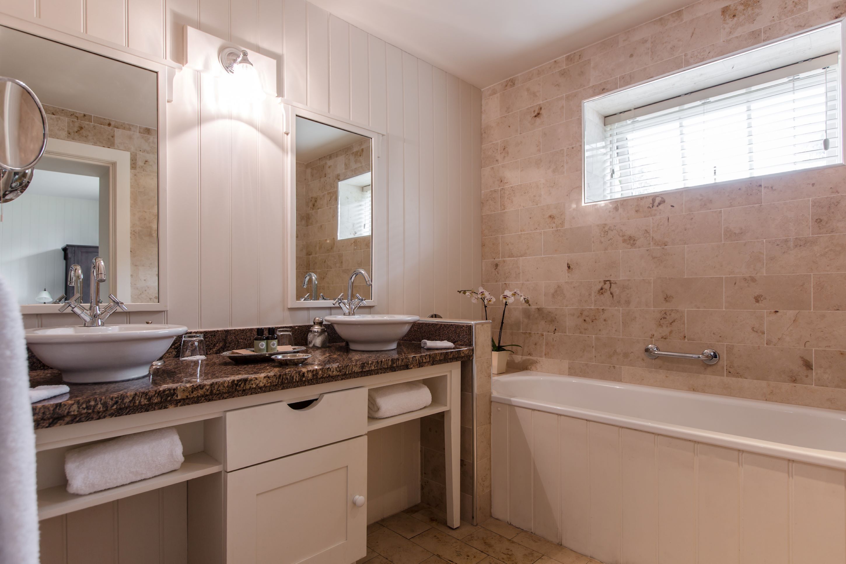 A modern bathroom with two sinks, a large mirror, and a bathtub.