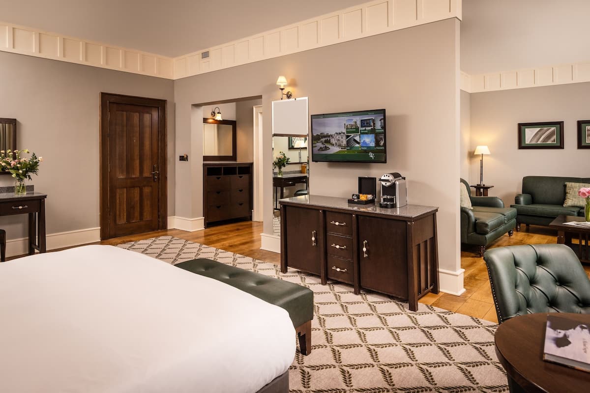 A hotel room with a large bed, a desk with a computer, a television, a green sofa, and a coffee machine.