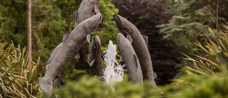 A sculpture of fish in a natural setting with water features and greenery.
