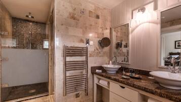 Un baño moderno con cabina de ducha de vidrio, toallero, dos lavamanos y un espejo grande.