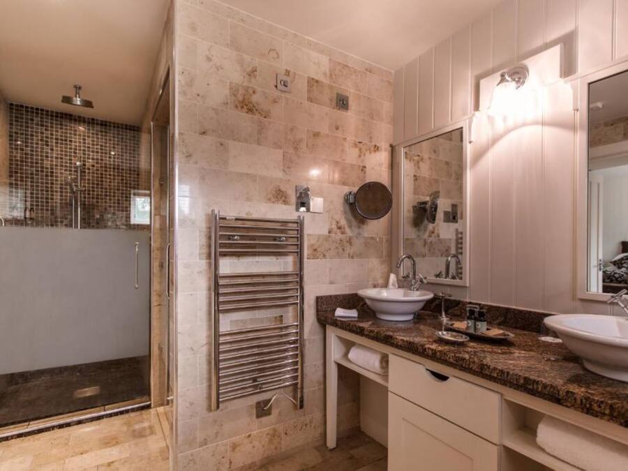Un baño moderno con cabina de ducha de vidrio, toallero, dos lavamanos y un espejo grande.