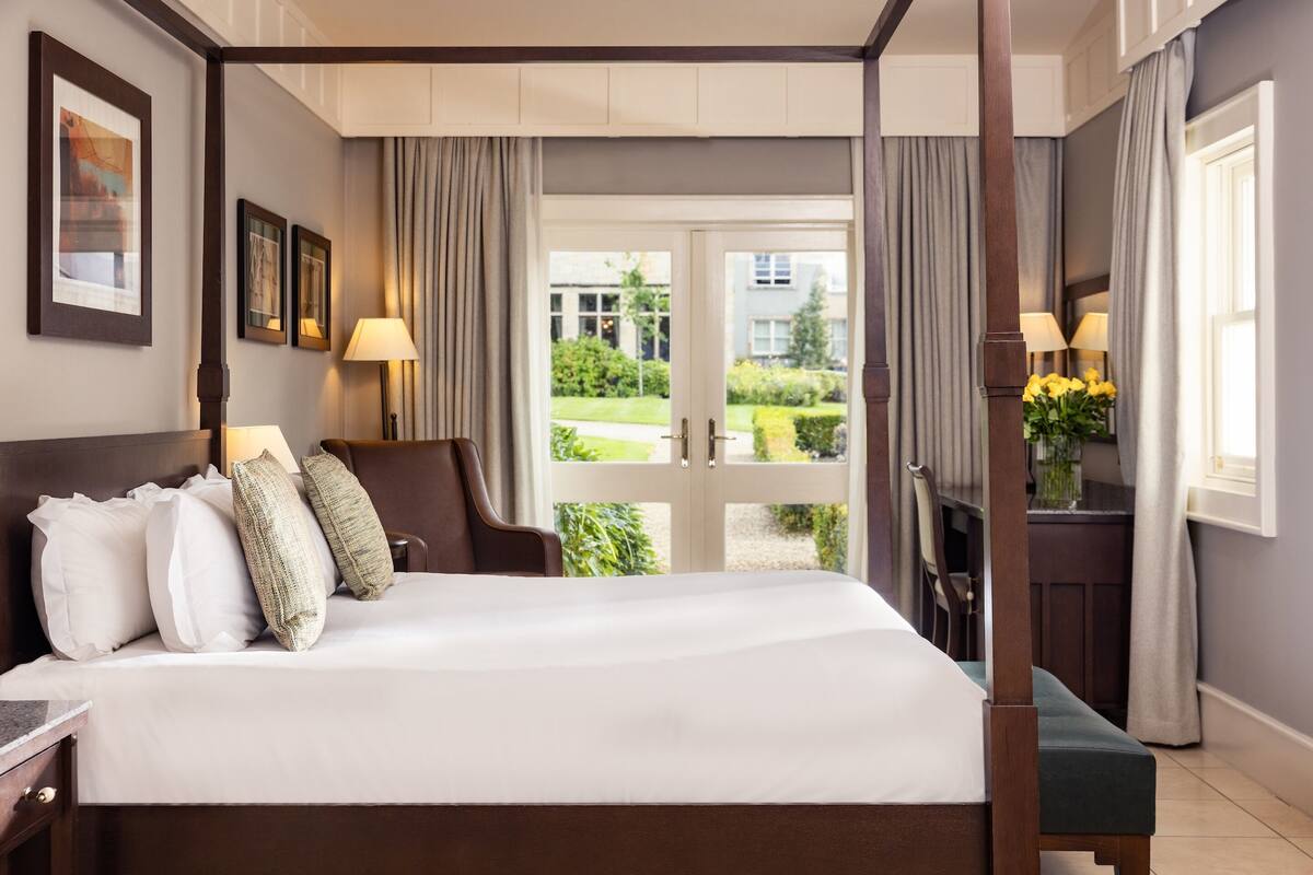A four-poster bed with a view of a garden through a glass door.