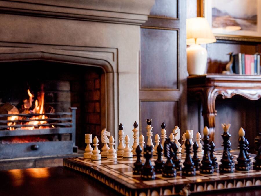 Un tablero de ajedrez dispuesto sobre una mesa de madera en una habitación con chimenea.
