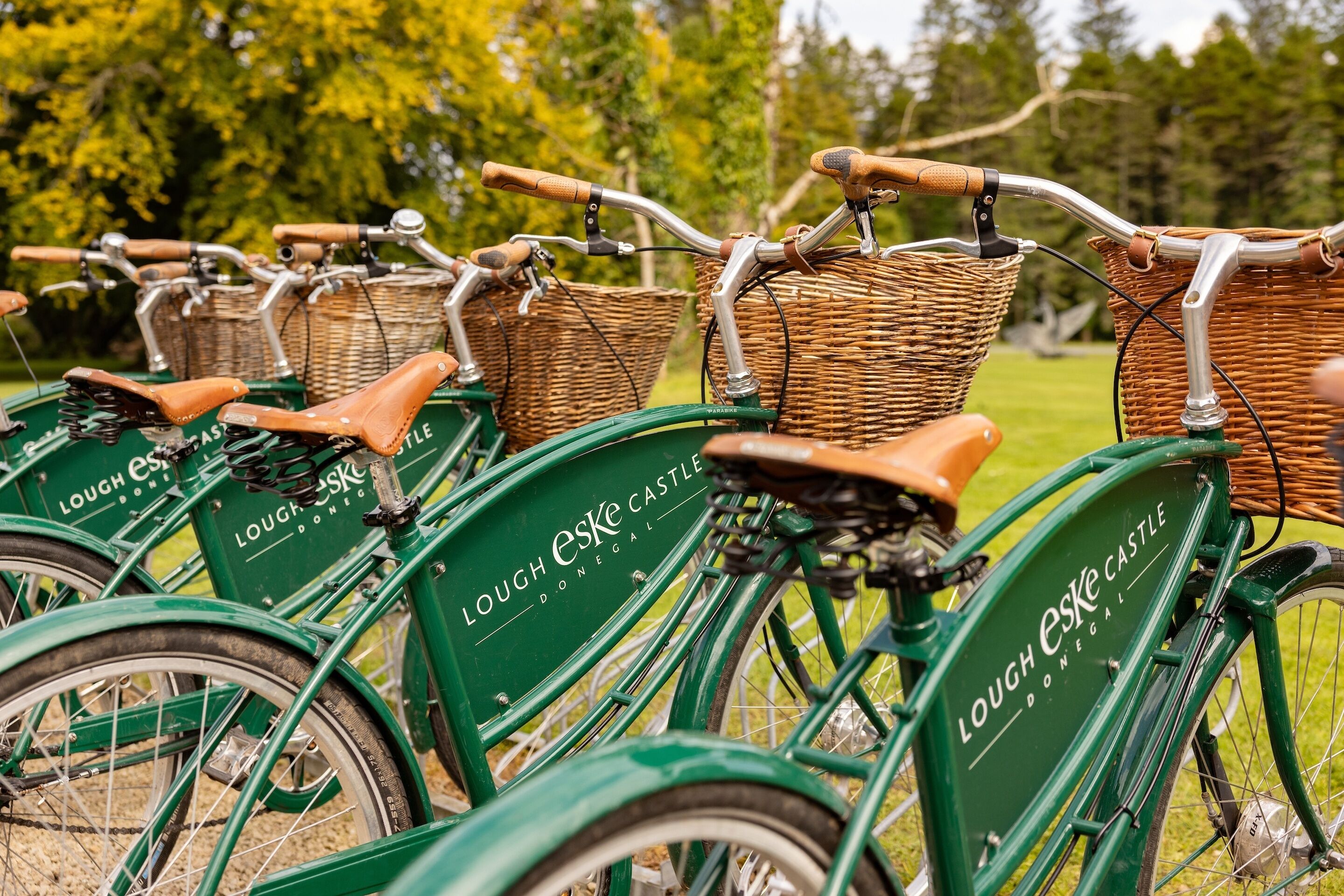 Una hilera de bicicletas verdes con cestas de mimbre y asientos de cuero, identificadas como "Lough Eske Castle".