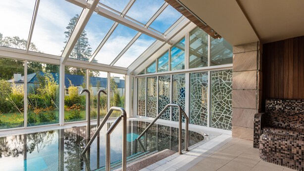 An indoor swimming pool with glass walls, a tiled floor, and a mosaic wall. - Lough Eske Castle (Donegal)