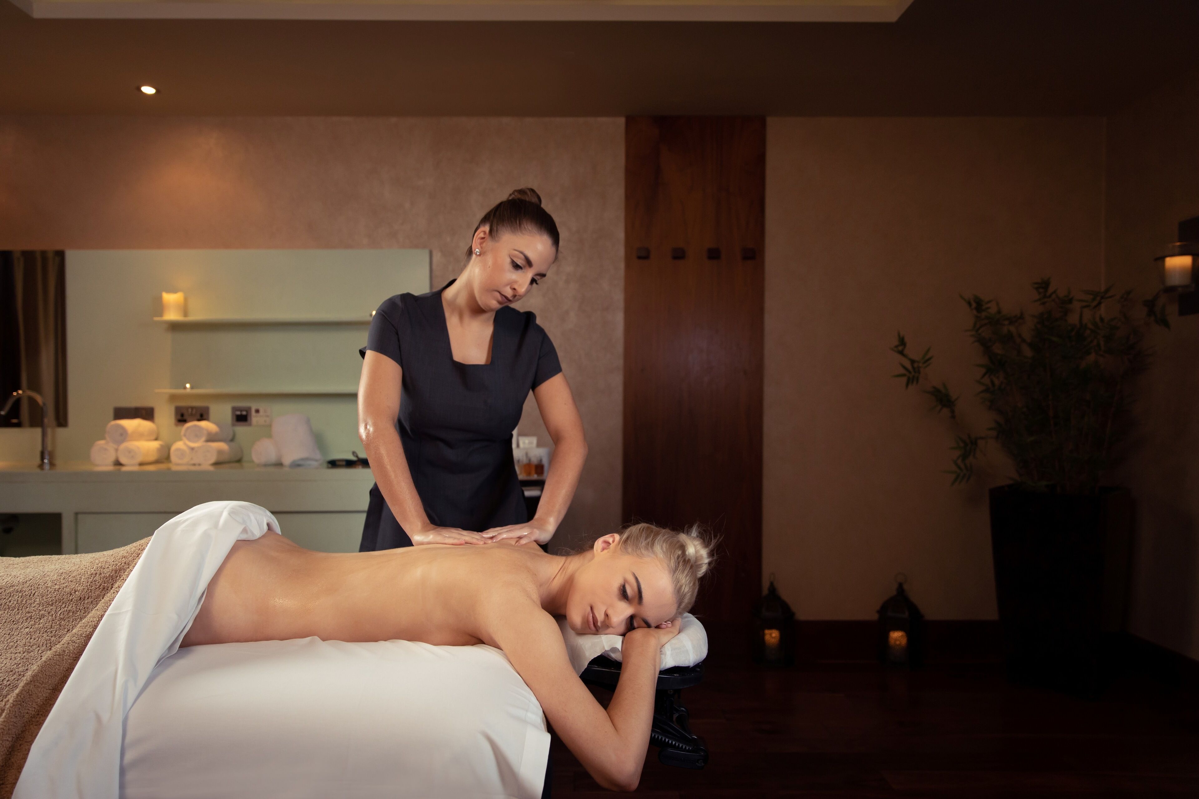 A massage therapy room with a massage table, a client receiving a back massage, and a therapist.