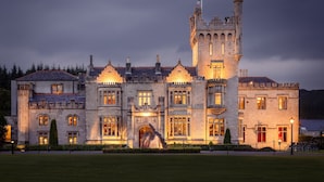 A large, historic stone building with multiple towers and arched windows, likely a castle or manor, with a well-maintained lawn in front. - Lough Eske Castle (Donegal)