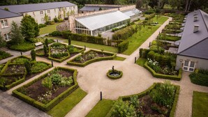 A large building with a glass greenhouse, surrounded by well-manicured gardens and a central circular lawn. - Lough Eske Castle (Donegal)
