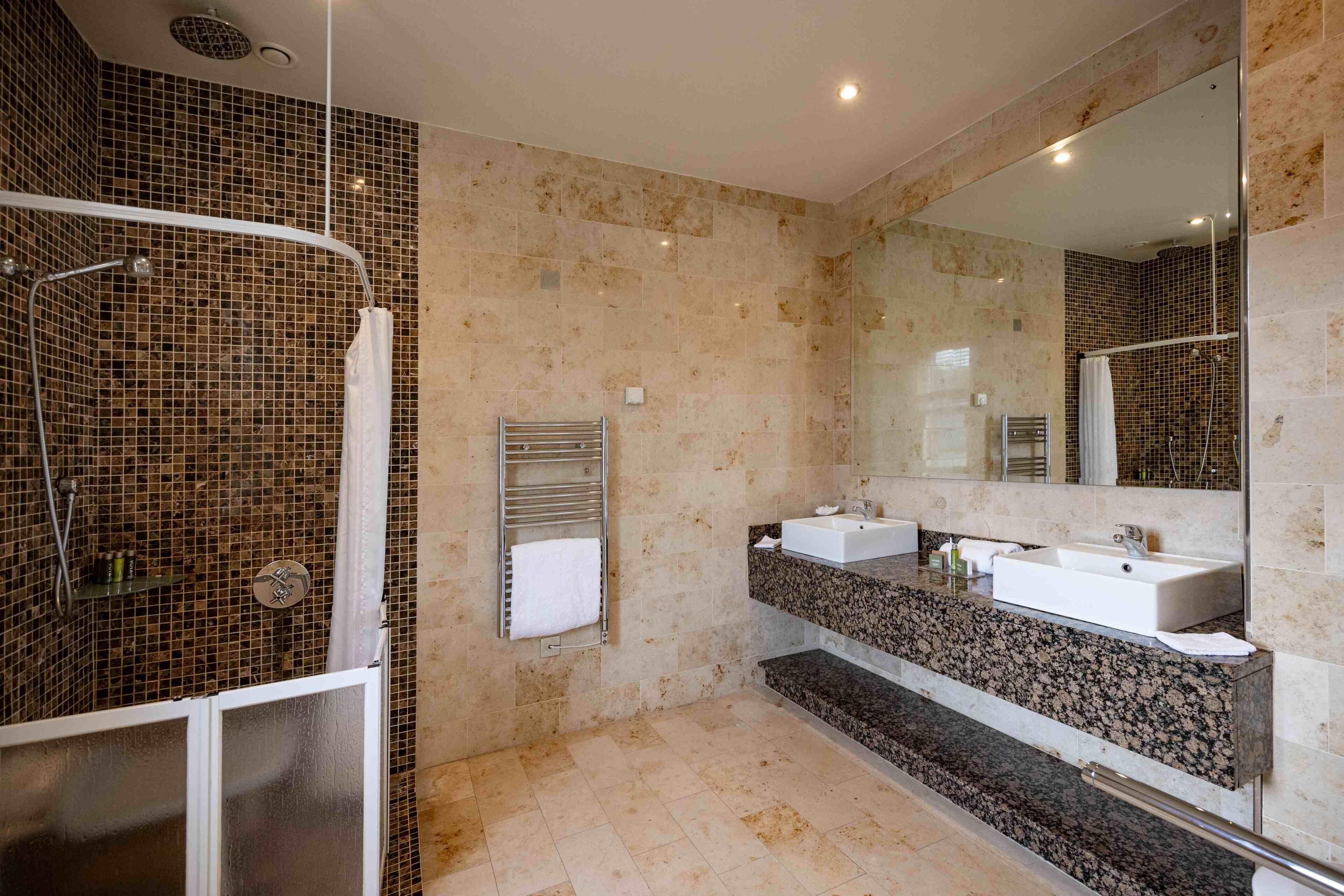 A modern bathroom with a glass-enclosed shower, two sinks, a large mirror, and a towel rack.