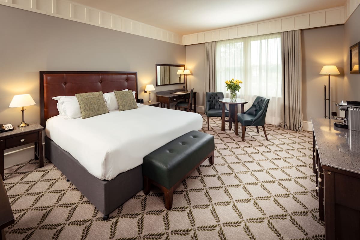 A hotel room with a large bed, a desk, a chair, and a small table with flowers.