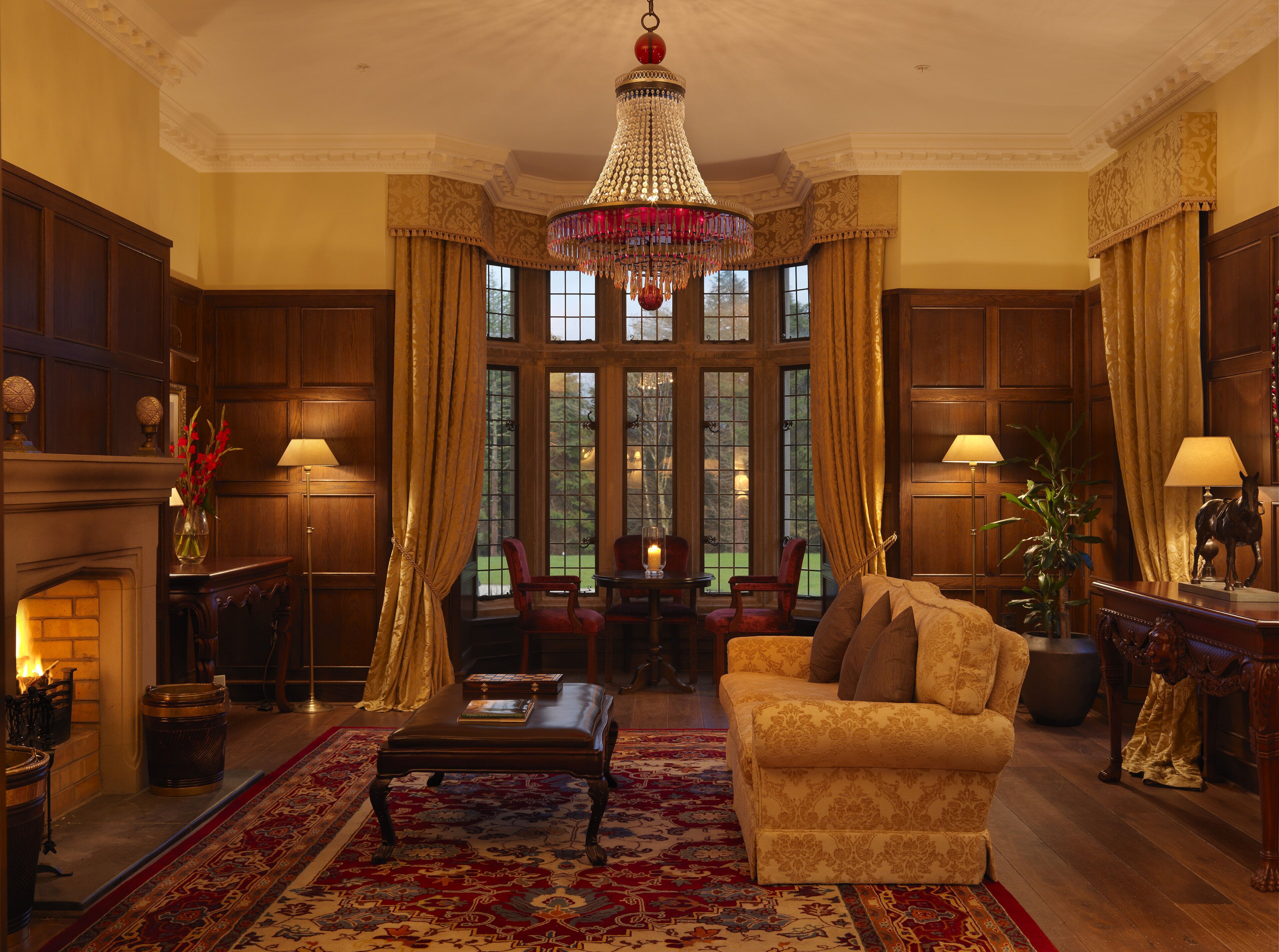 A formal room with a chandelier, wooden paneling, a fireplace, and a large window with curtains.