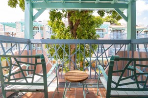 A gazebo with a swing chair, surrounded by a metal fence and a tree.